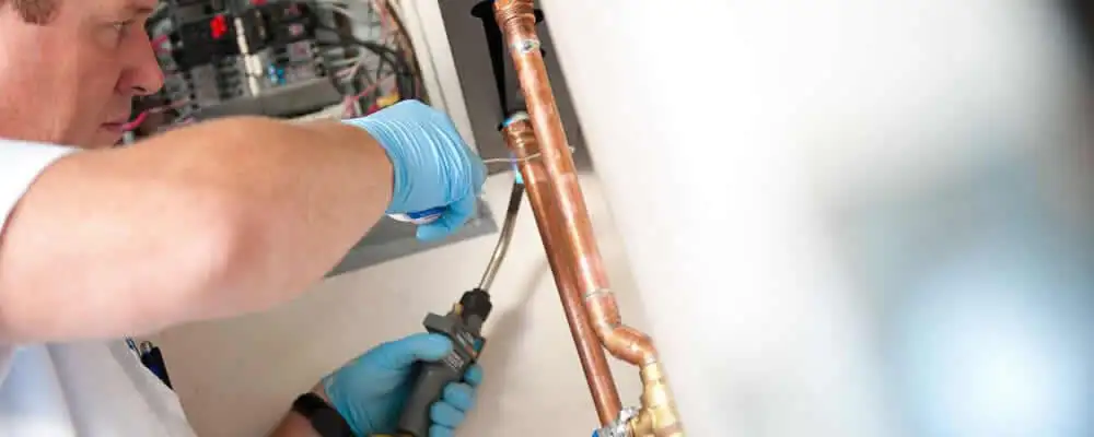 Water heater repair technician testing copper pipe connections and controls in Green Bay, WI